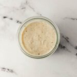 Overhead view of finished white gravy in a jar on marble surface.