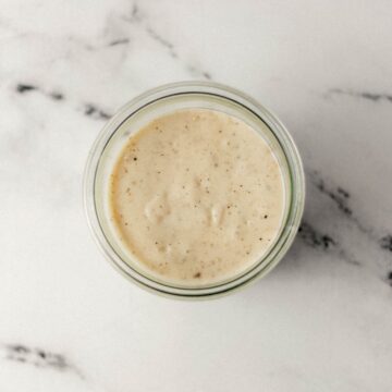 Overhead view of finished white gravy in a jar on marble surface.