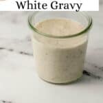 Close up side view of white gravy in a glass jar on marble surface on pin with text overlay.