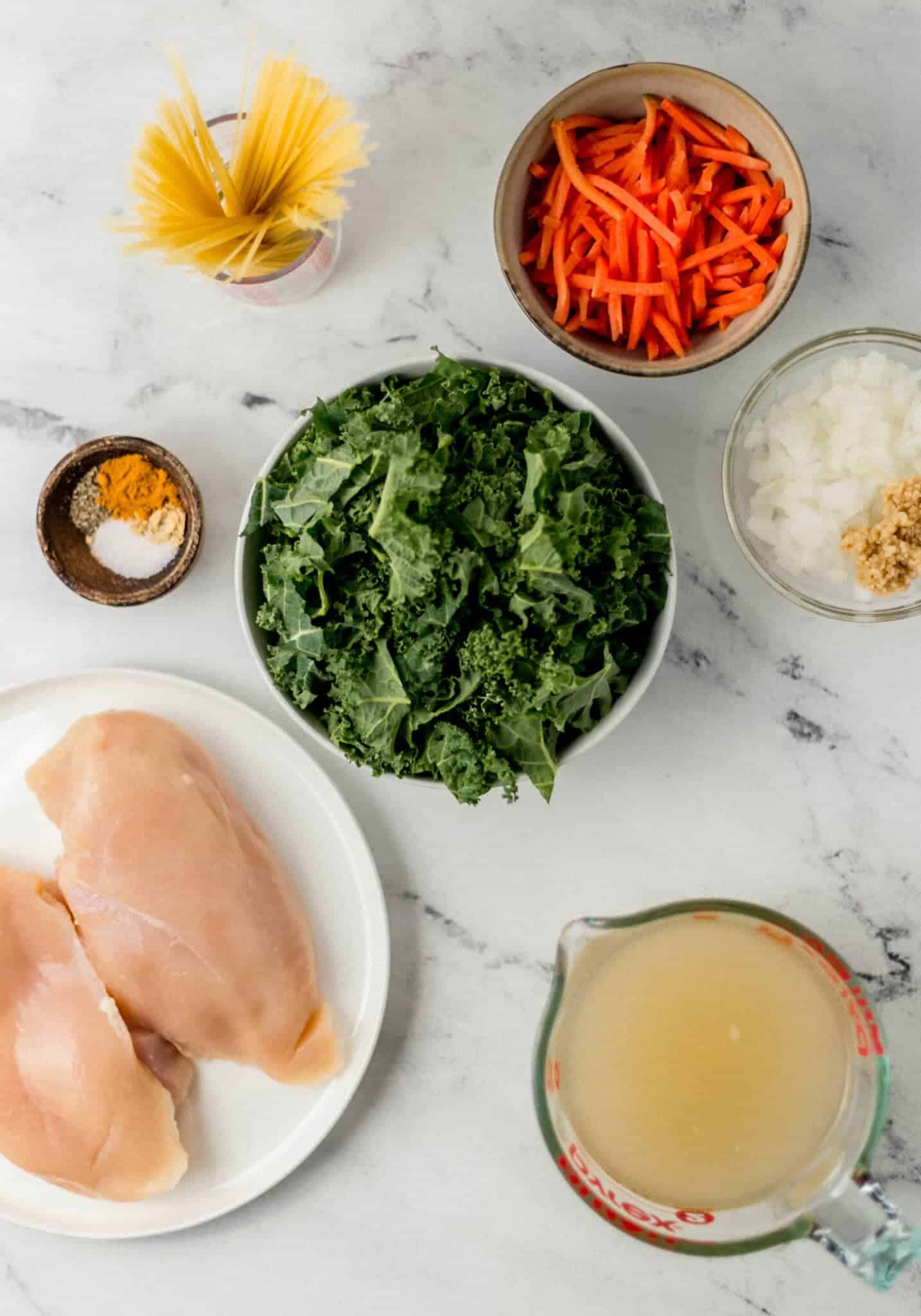 overhead view of ingredients needed to make chicken noodle soup in separate bowls