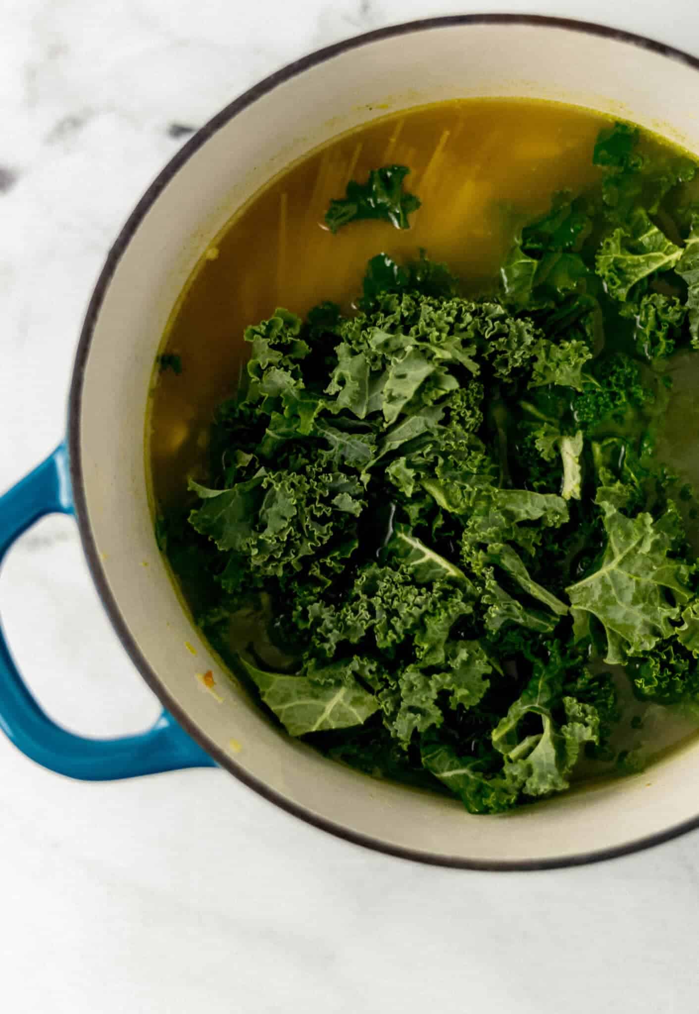 kale and noodles added to soup in large pot 