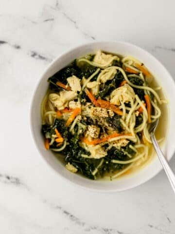 overhead view of single white bowl of chicken noodle soup with spoon in it.