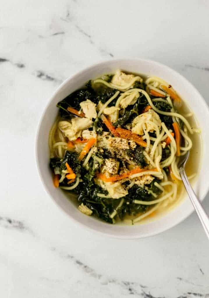 overhead view of single white bowl of chicken noodle soup with spoon in it.