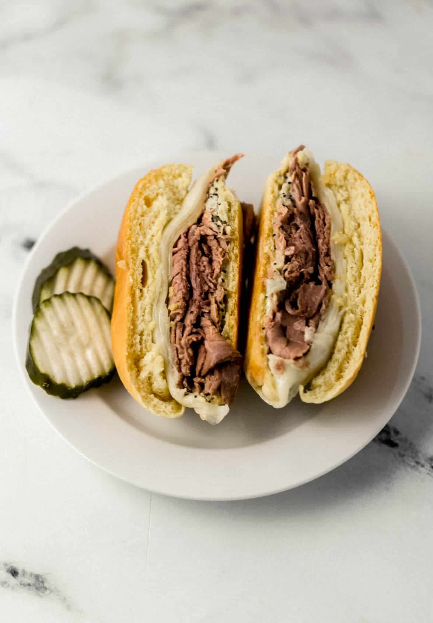 finished sandwich cut in half on white plate with pickle slices 