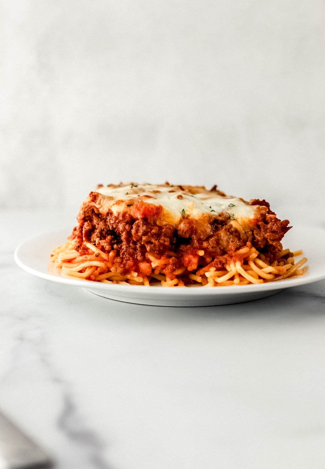 Close up side view of piece of baked spaghetti on white plate. 