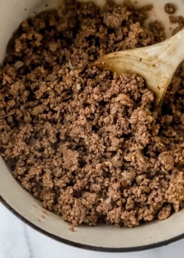 Overhead view of meat, onion, and garlic in pot with wooden spoon.