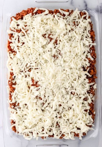 Meatsauce and cheese added to baking dish with other ingredients.