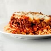 Close up side view of spaghetti on a plate on pin with text overlay.