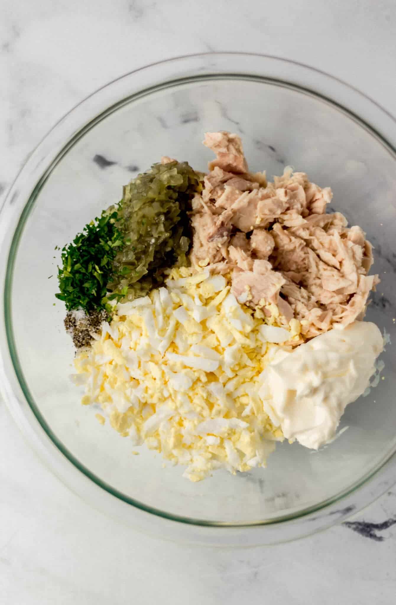 ingredients to make tuna salad in a glass mixing bowl 