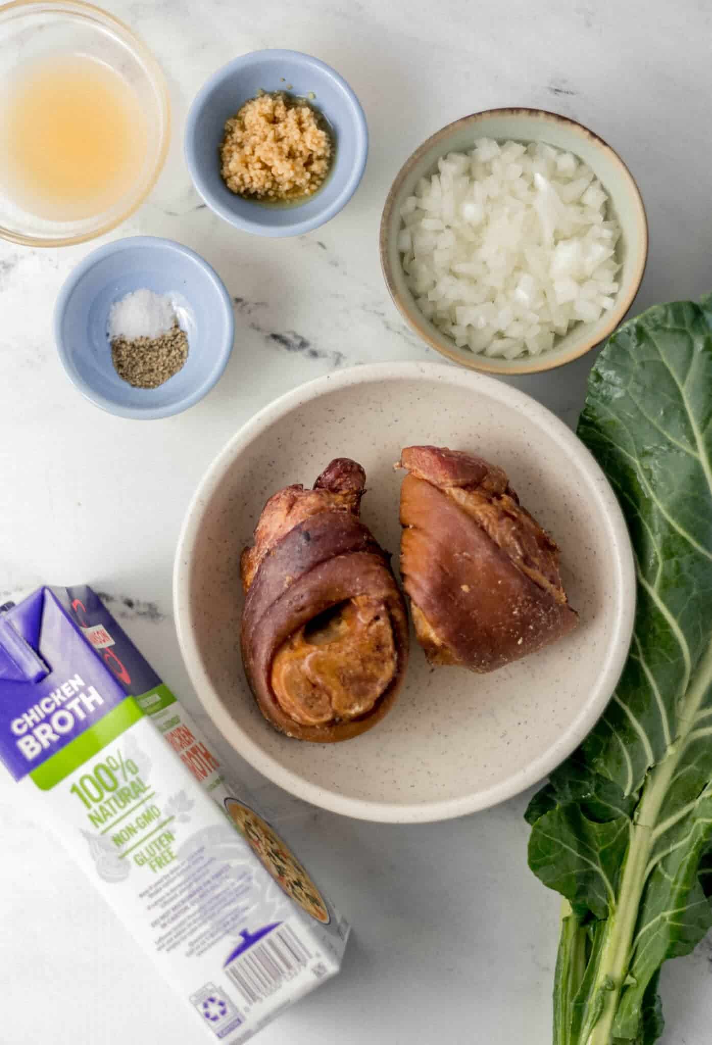 overhead view of ingredients needed to make collards with ham hock in separate bowls and containers 
