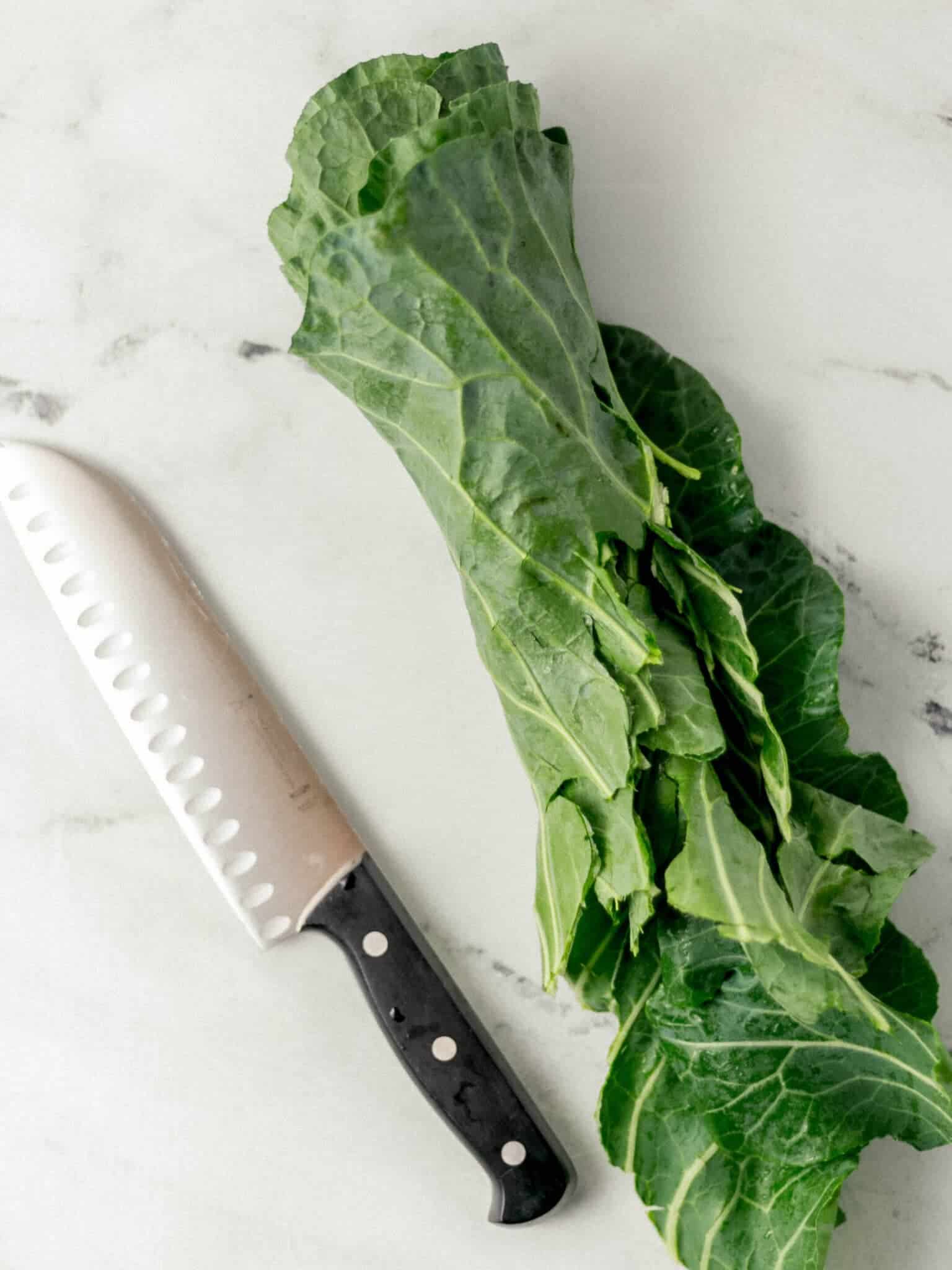 collard greens rolled together beside a knife 