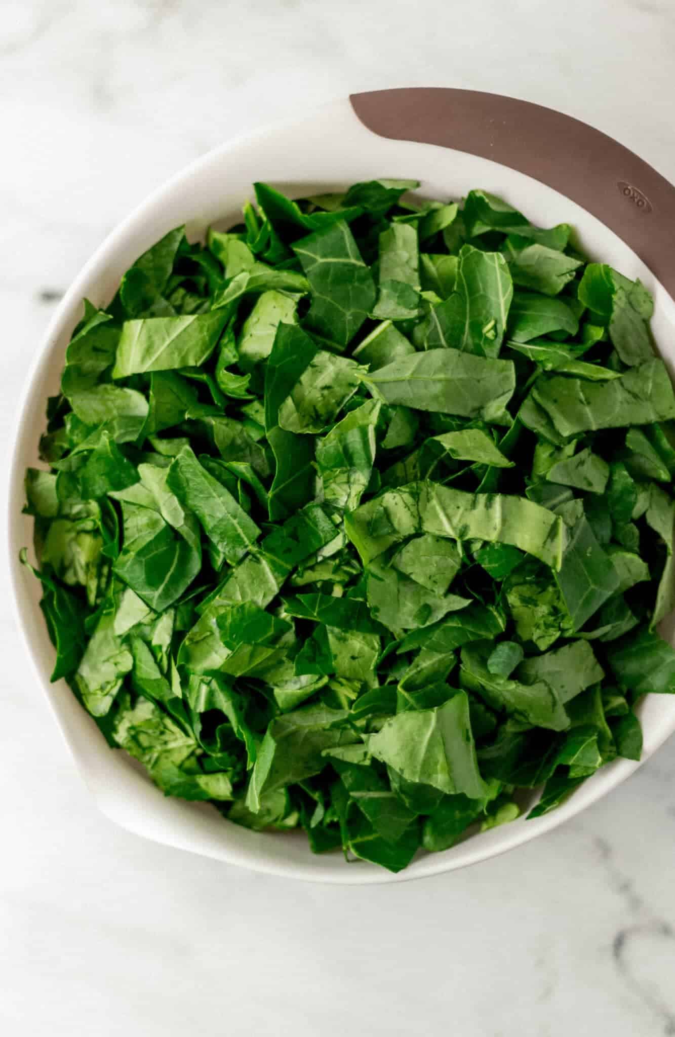 cleaned and cut up fresh collard greens in large white bowl 