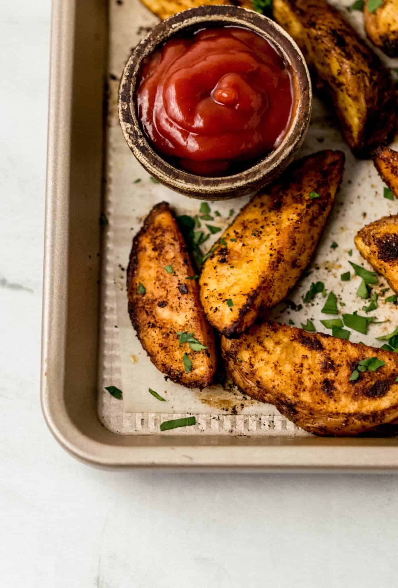 baked potato wedges on baking sheet with small bowl of ketchup 