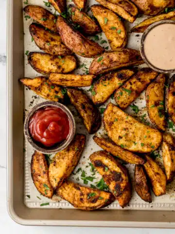 overhead view of finished potato wedges on parchment lined baking sheet with small wooden bowls of condiments