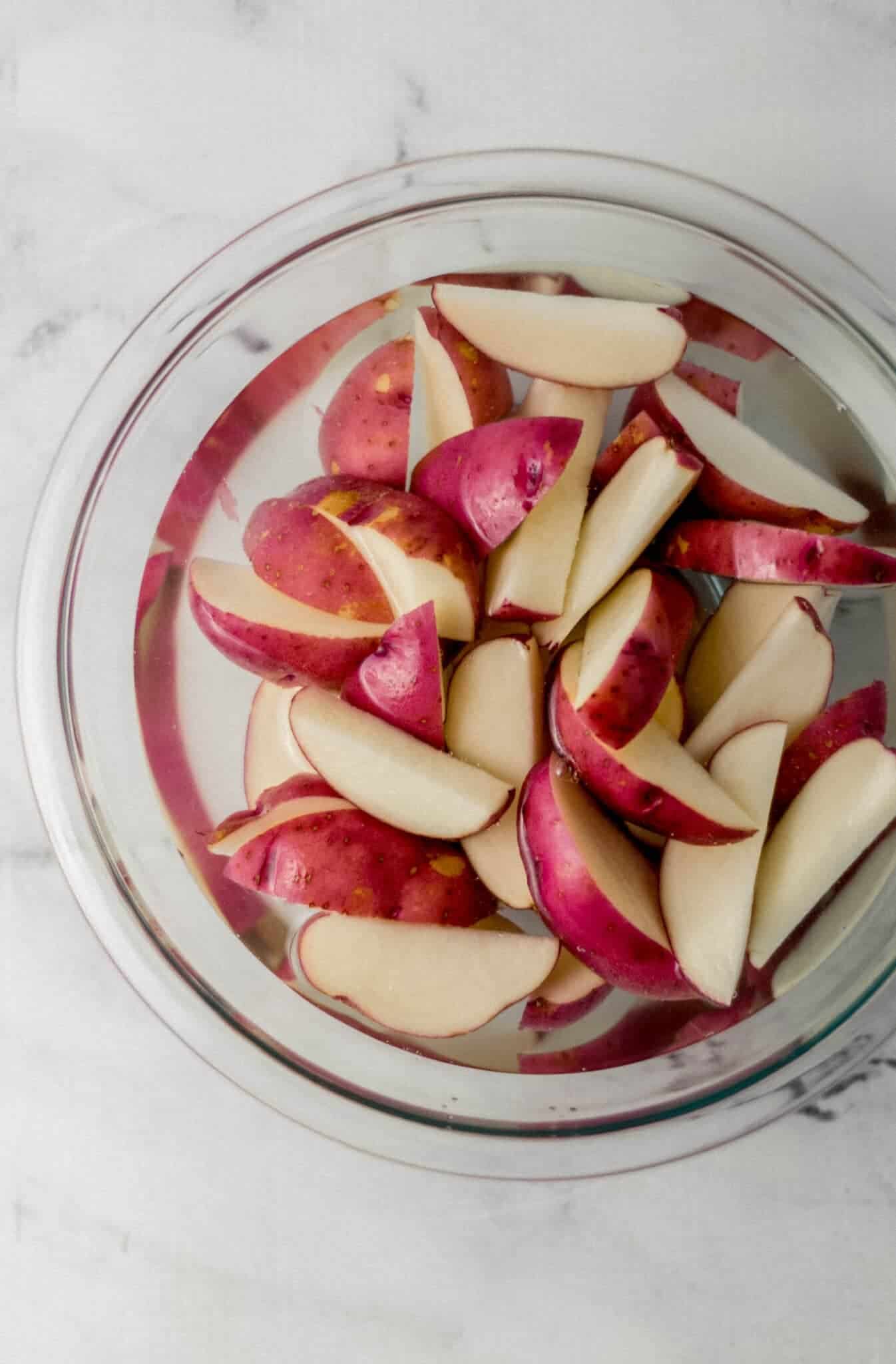 cut up potatoes in glass bowl with water 