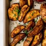 Close up view of potatoes on baking sheet with small bowl of ketchup.