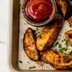 Close up view of finished potatoes on baking sheet with wooden bowl of ketchup.