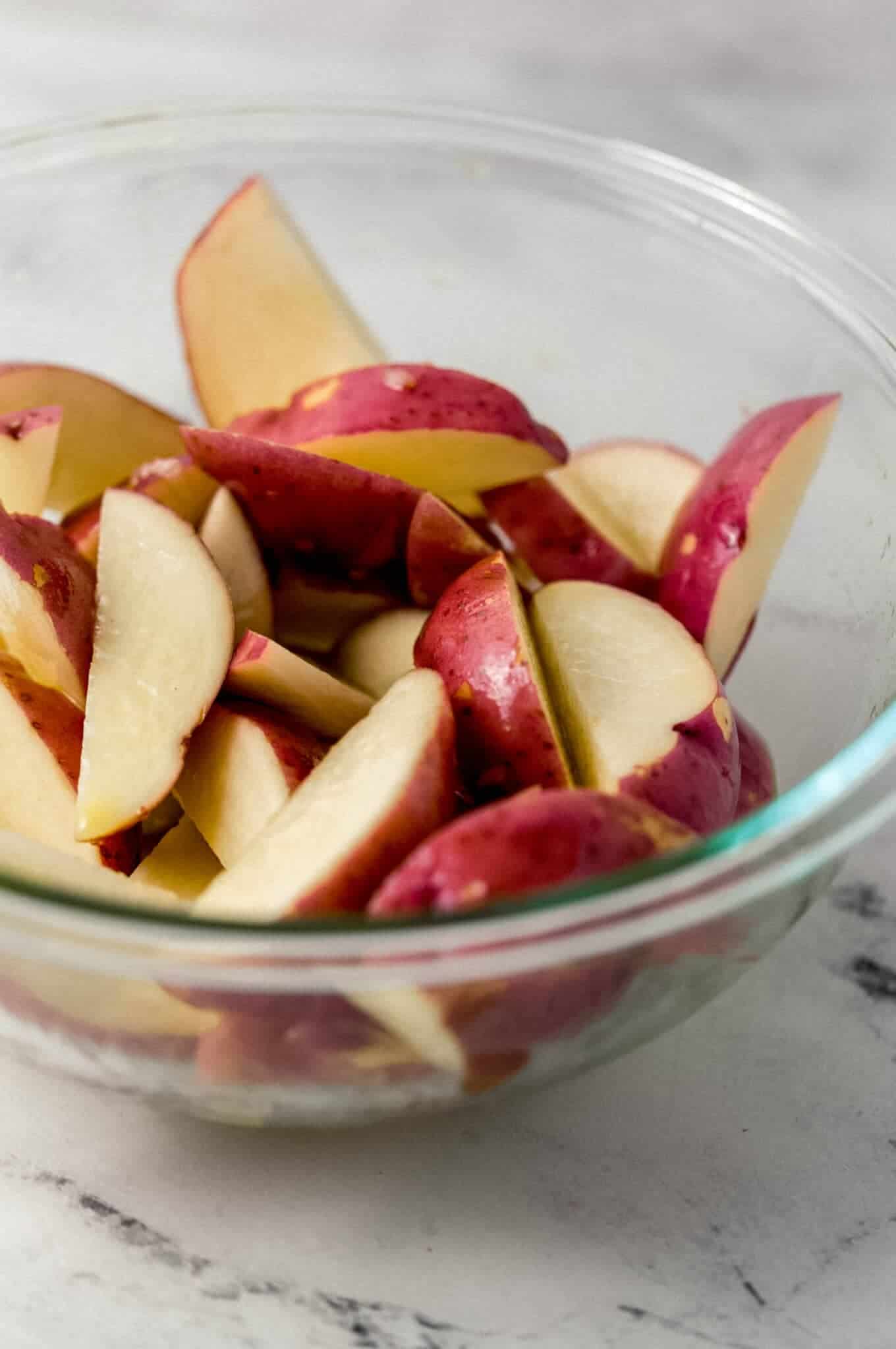 close up side view of cut up potatoes in glass bowl with oil