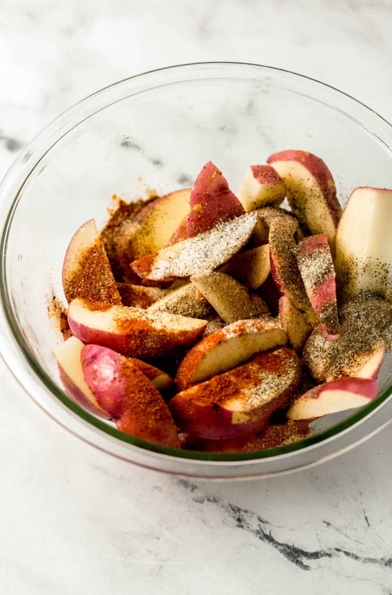 seasoning added to bowl with cut up potatoes 