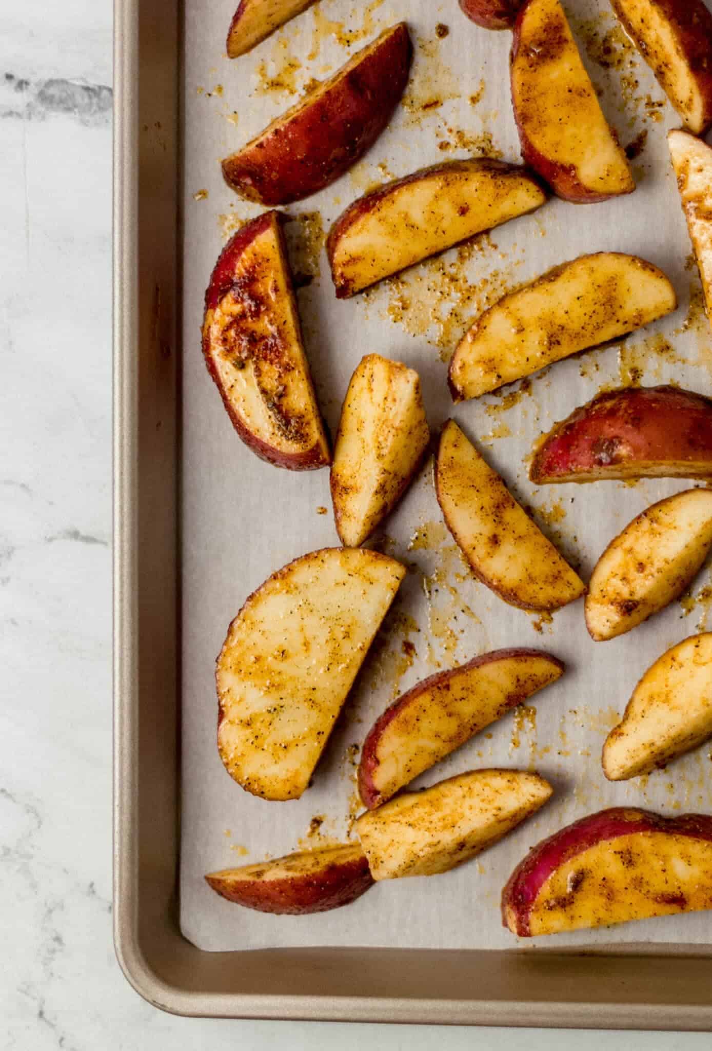 seasoned unbaked potatoes on parchment lined baking sheet 
