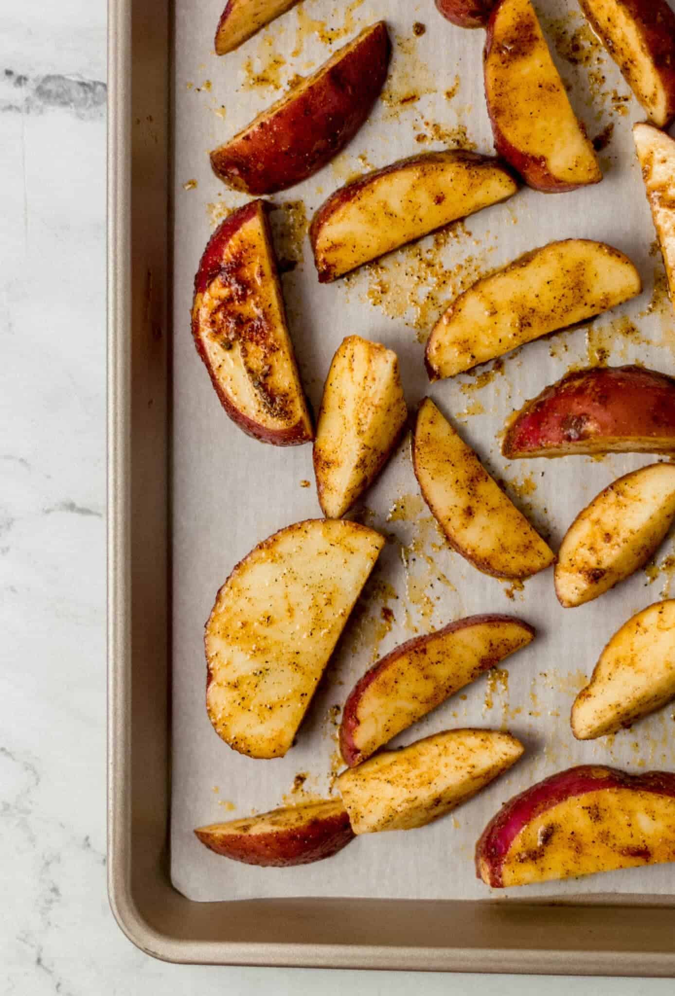 seasoned unbaked potatoes on parchment lined baking sheet