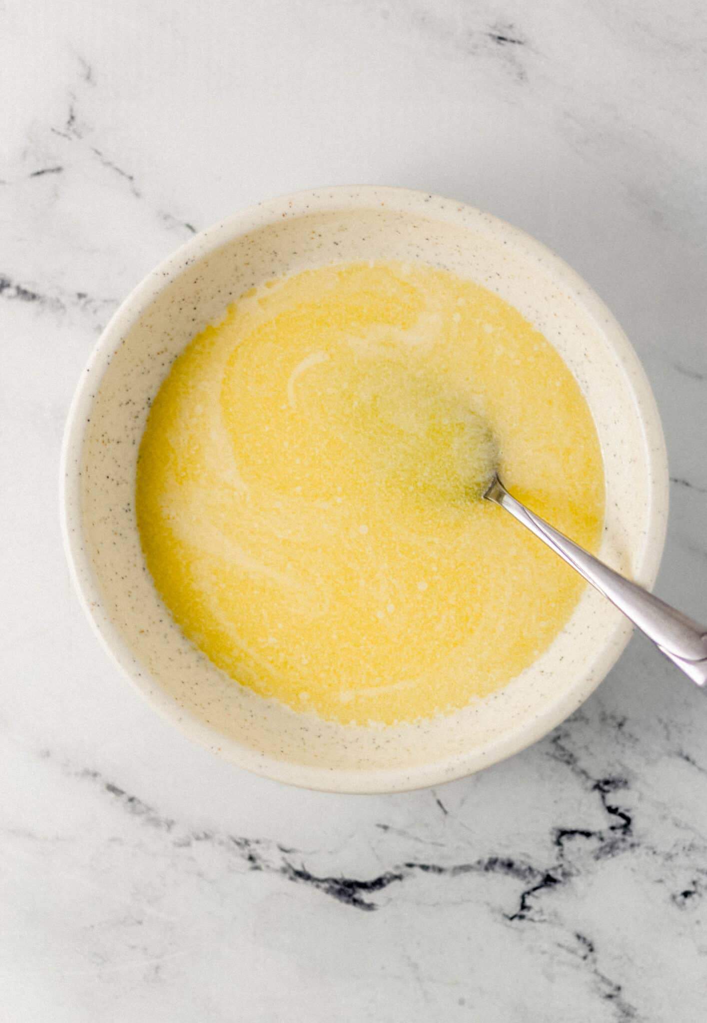 melted butter in white speckled bowl with spoon in it