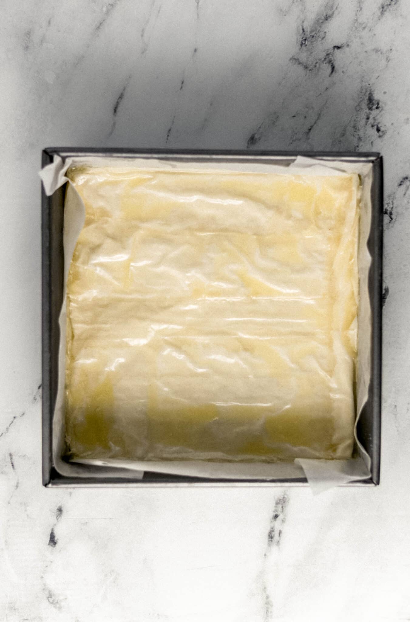 phyllo dough layered with melted butter in parchment lined square baking pan
