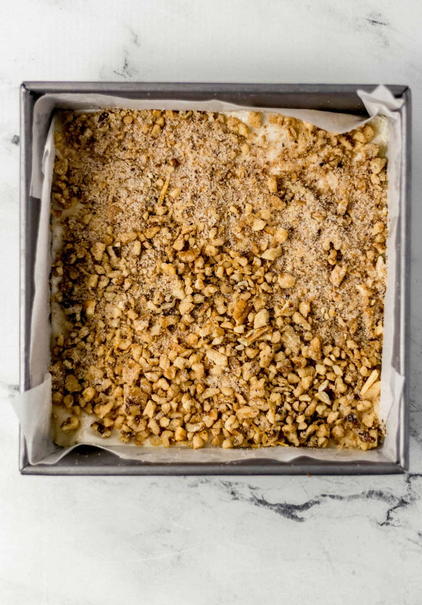 chopped walnut mixture added to the top of the buttered dough in the parchment lined square baking pan 