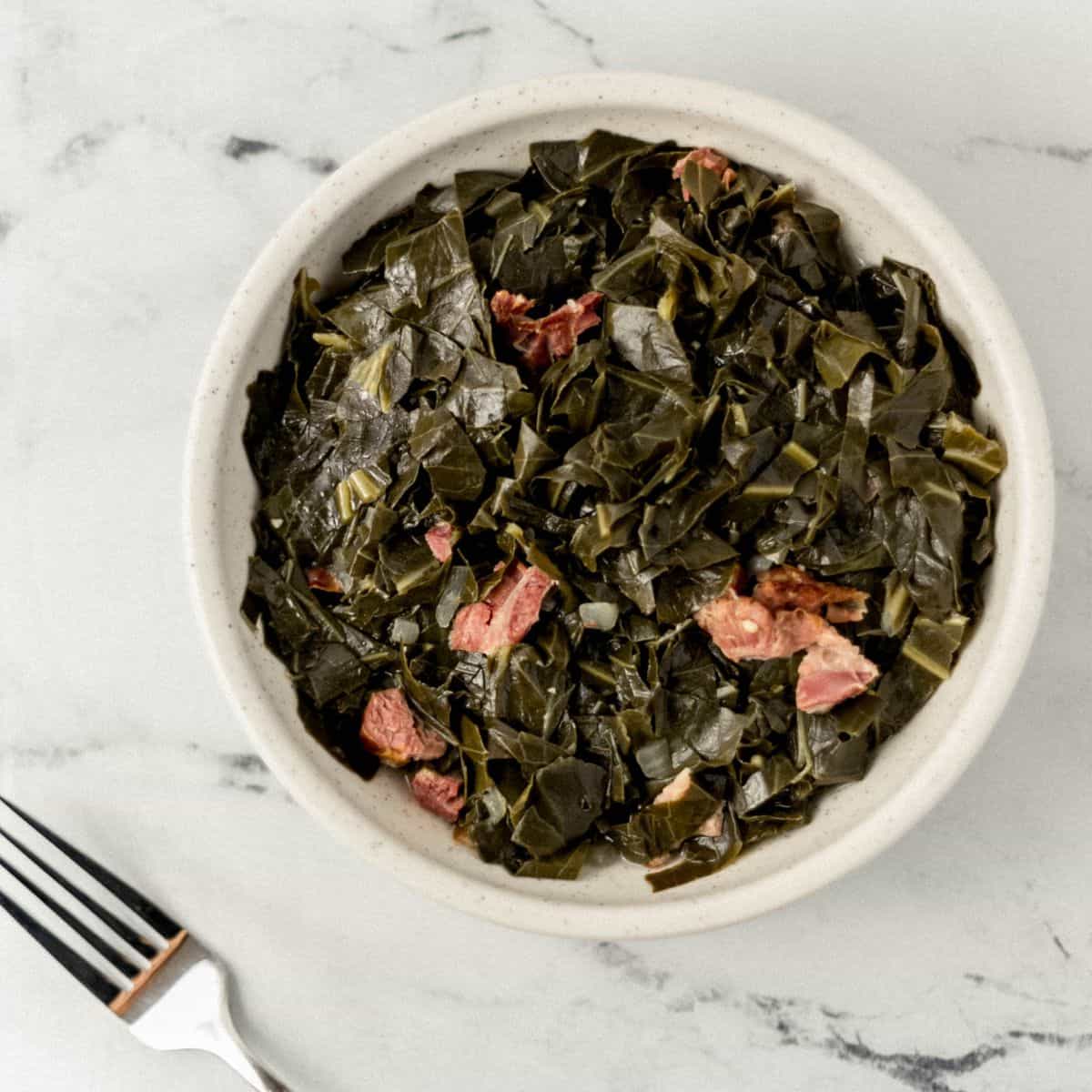 Overhead view of white bowl with greens in it by a fork.