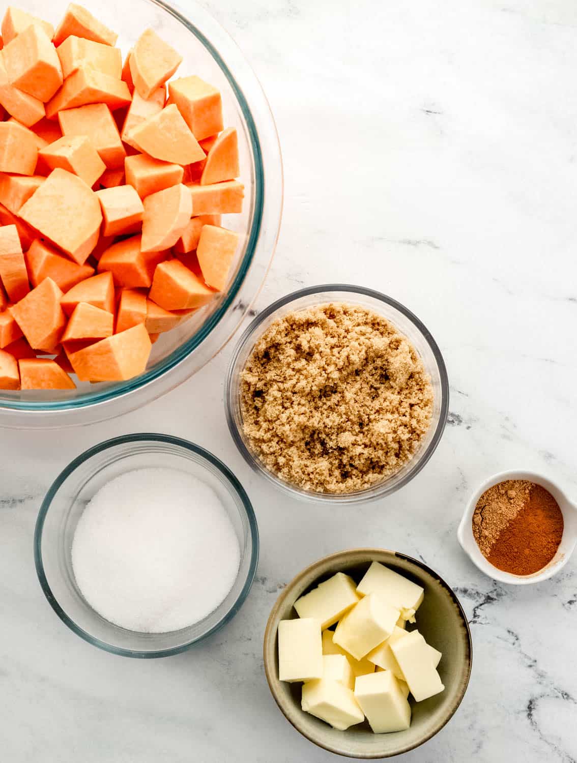 Overhead view of ingredients needed to make yams in separate bowls on marble surface. 