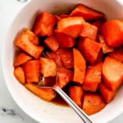 Finished single serving of yams in white bowl with spoon in it.