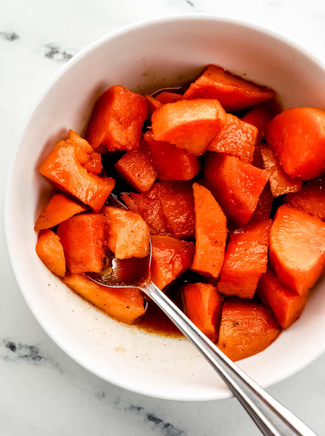 Single serving of finished yams in white bowl with spoon in it. 