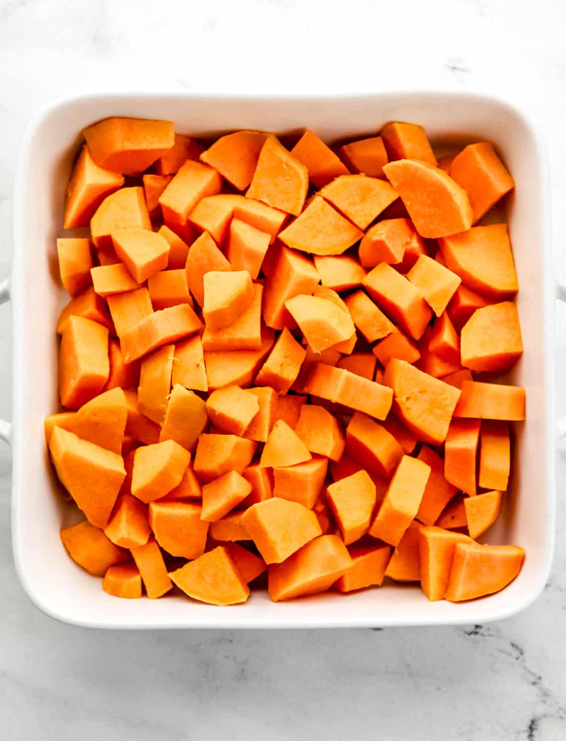 Boiled sweet potatoes in large white baking dish on marble surface. 