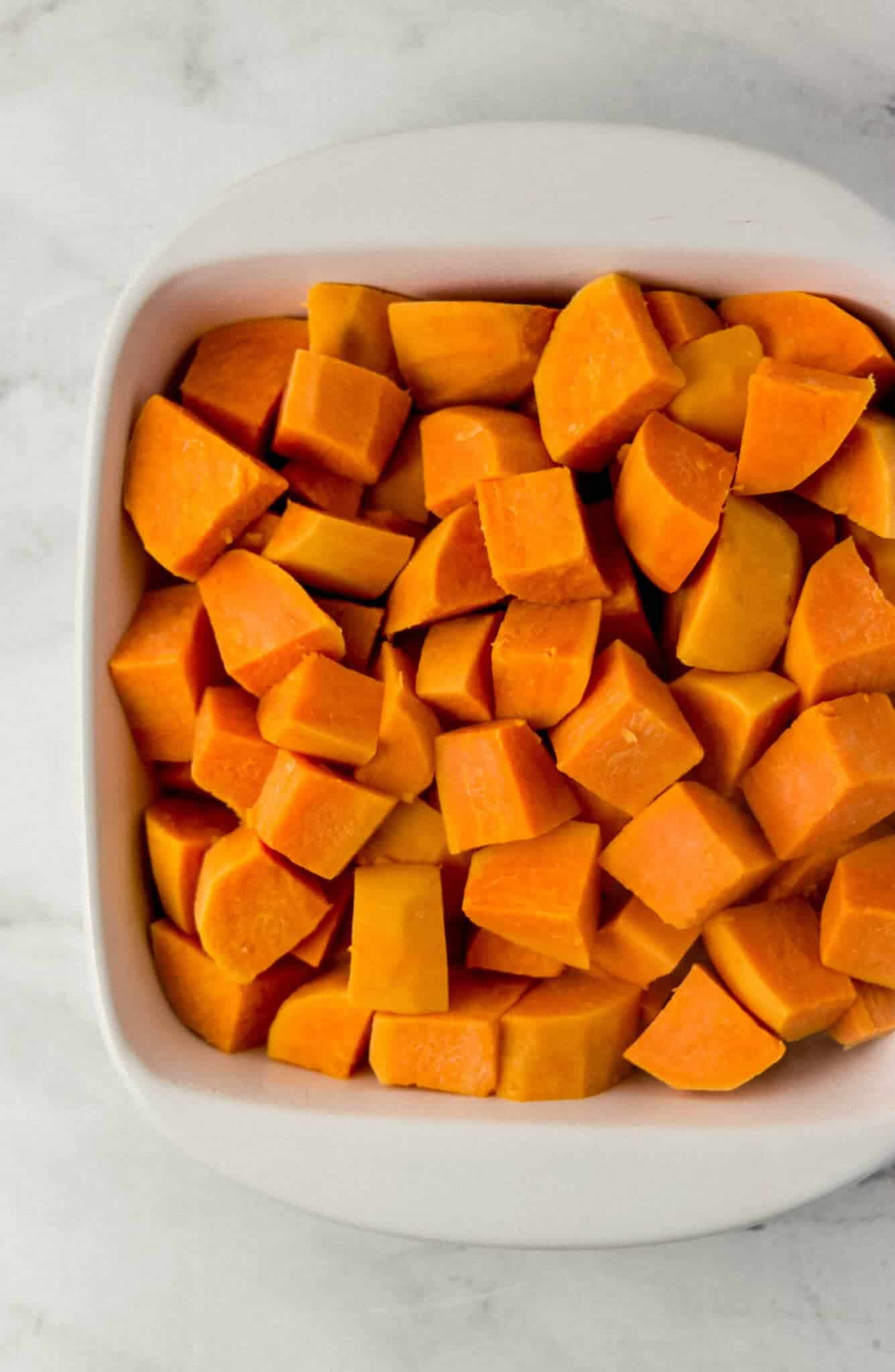 cooked sweet potatoes pieces added to white square baking dish 