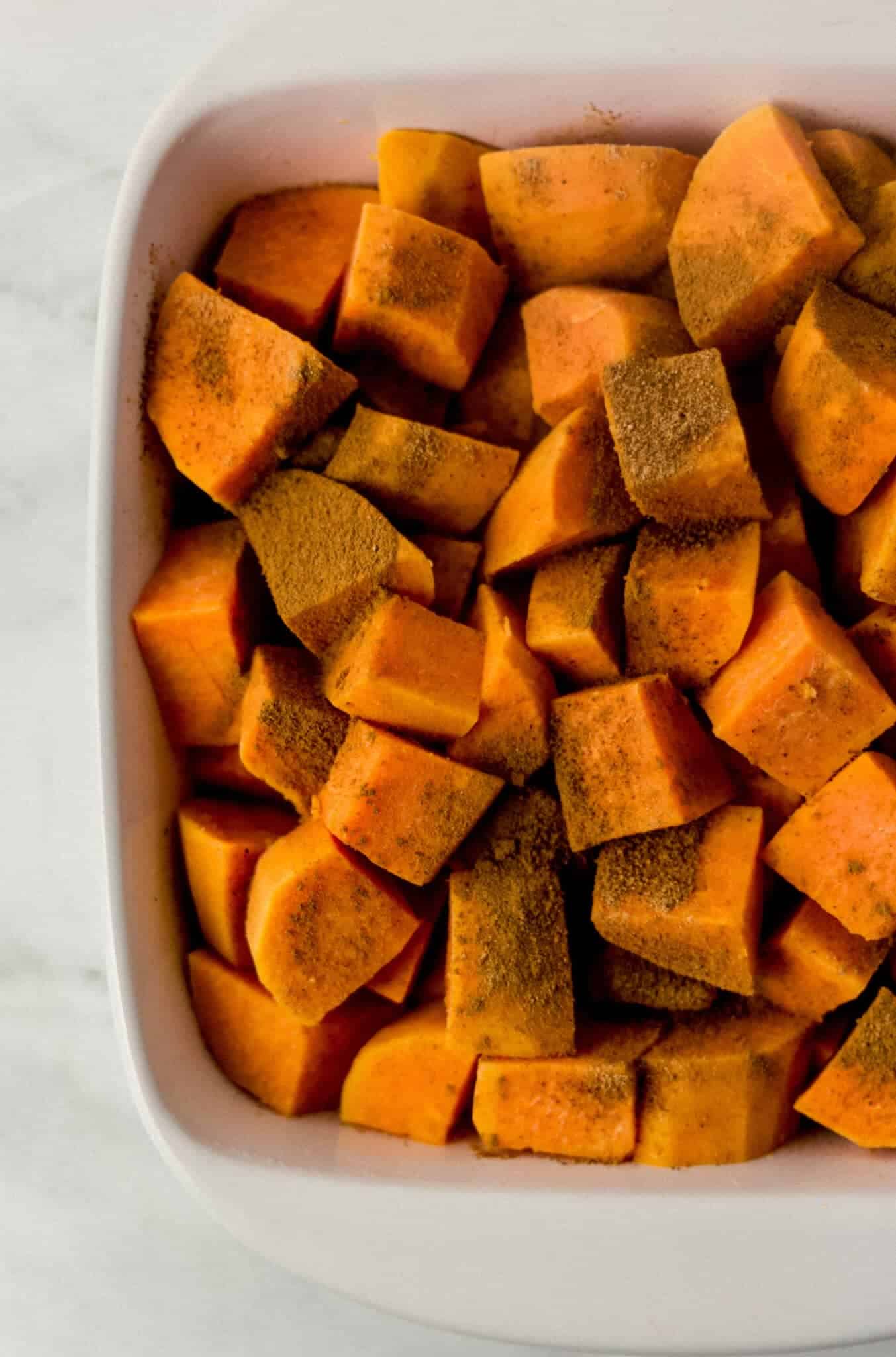 cooked sweet potatoes added to white square baking dish and topped with cinnamon and nutmeg