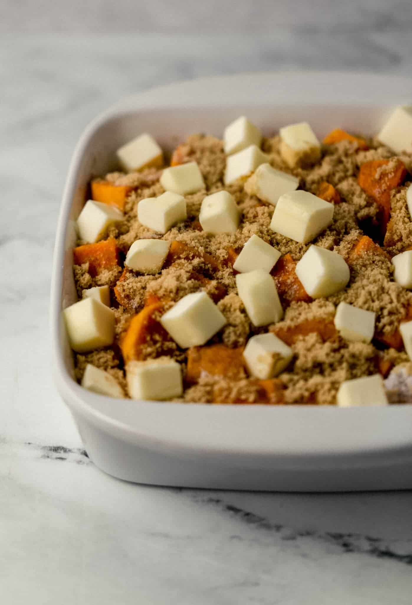 close up side view of sweet potatoes topped with cubes of butter in baking dish 