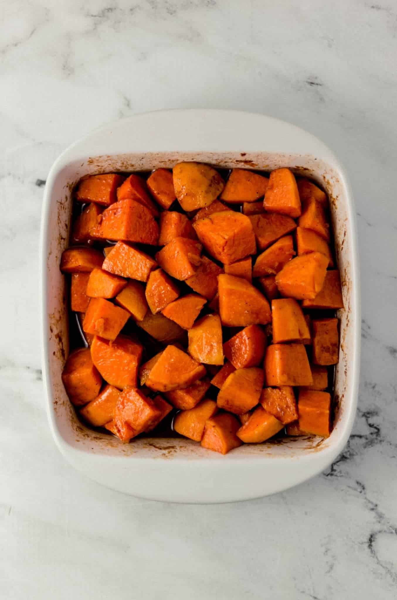 overhead view of finished candied yams in square white baking dish on marble surface 