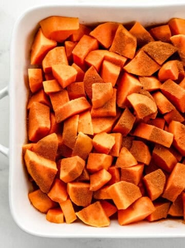 Cinnamon and nutmeg added to parboiled sweet potatoes in baking dish.