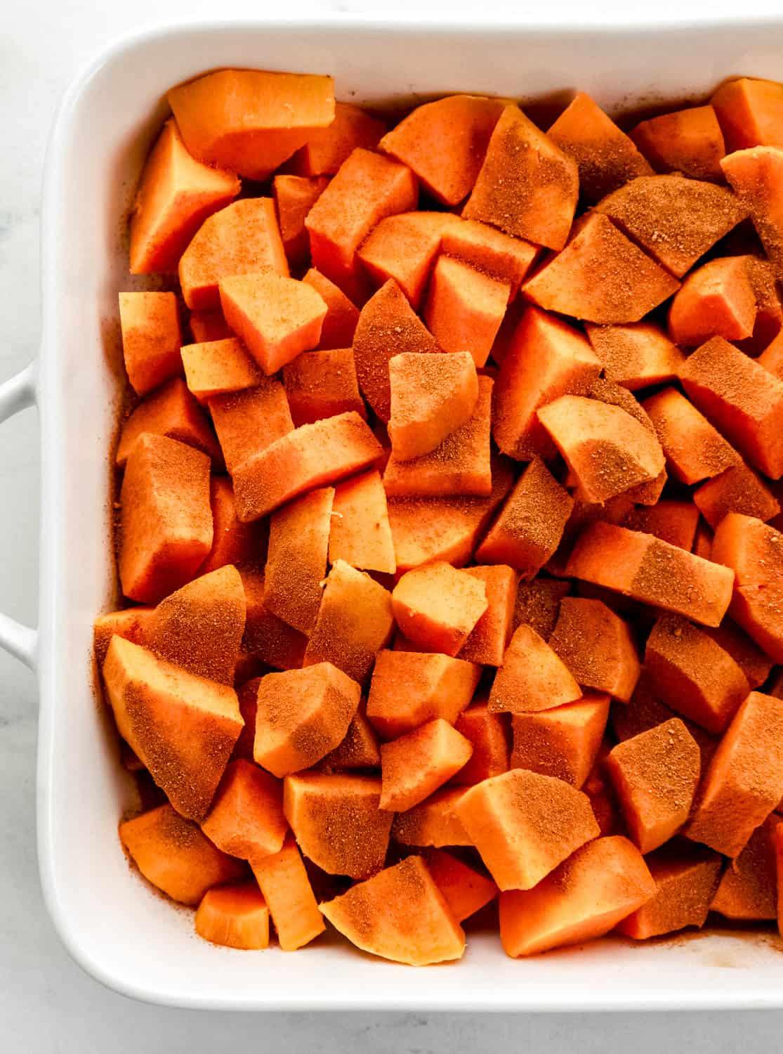 Boiled sweet potatoes in baking dish topped with cinnamon and nutmeg. 