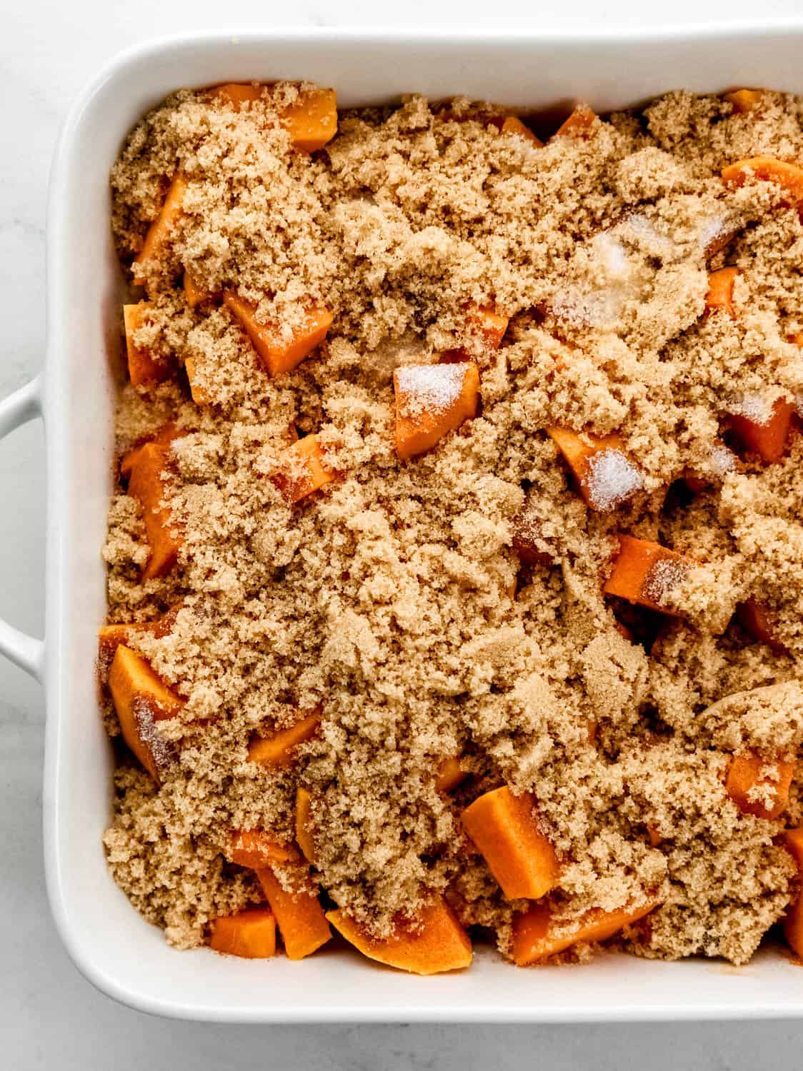 Sweet potatoes topped with granulated sugar and brown sugar in baking dish. 