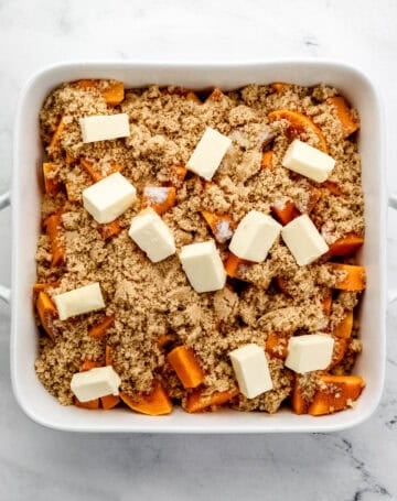 Cubed butter added on top of the other yam ingredients in the white baking dish.
