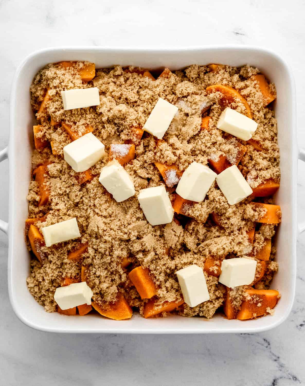 Cubed butter added to the top of the other yam ingredients in a white baking dish. 