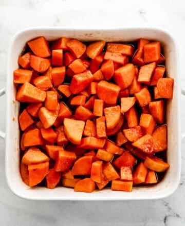 Overhead view of baked yams in white baking dish on marble surface.