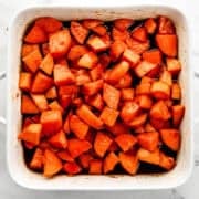 Overhead view of finished candied yams in square white baking dish on marble surface.