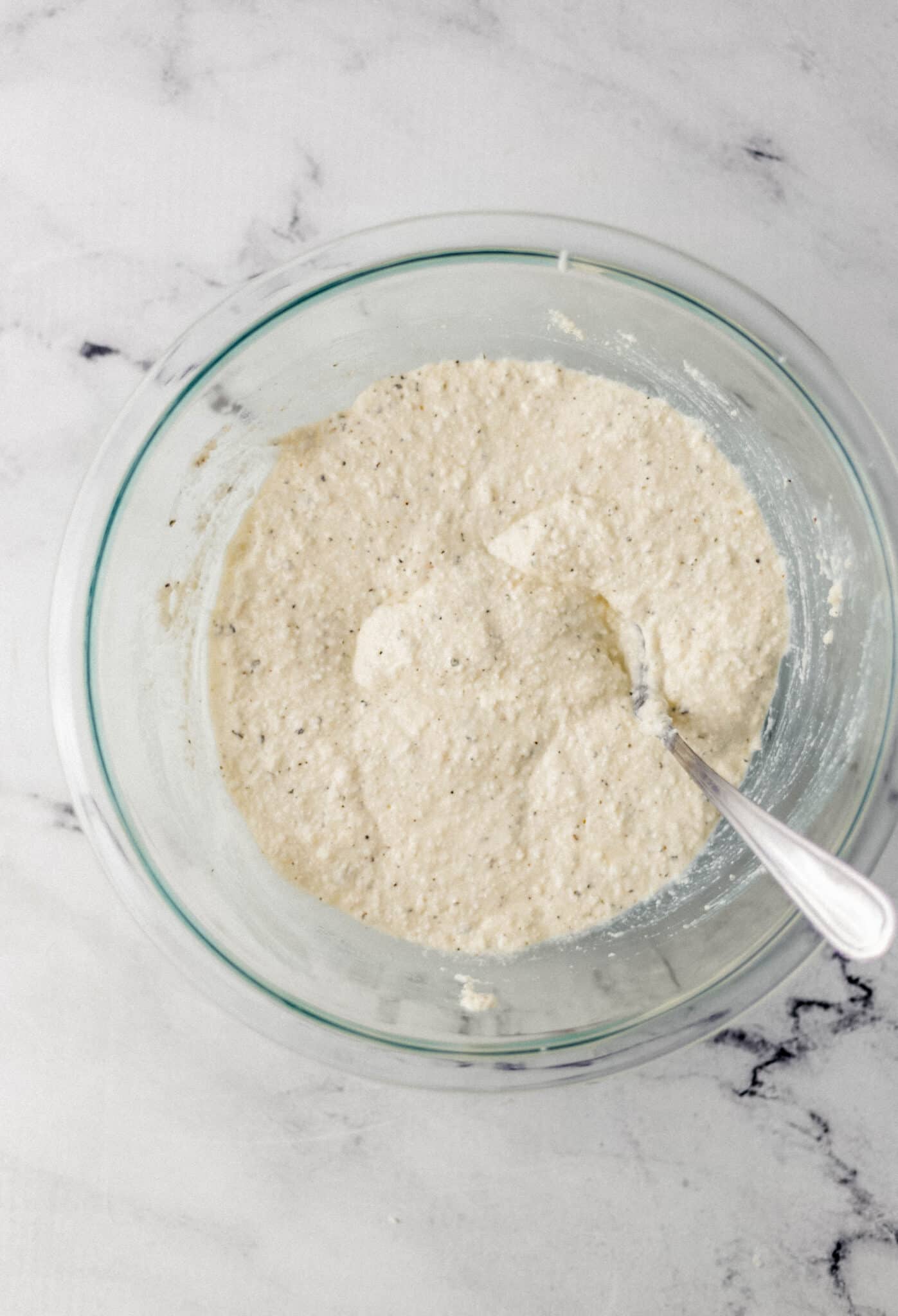 ricotta, parmesan, egg, and seasoning combined in glass mixing bowl with spoon