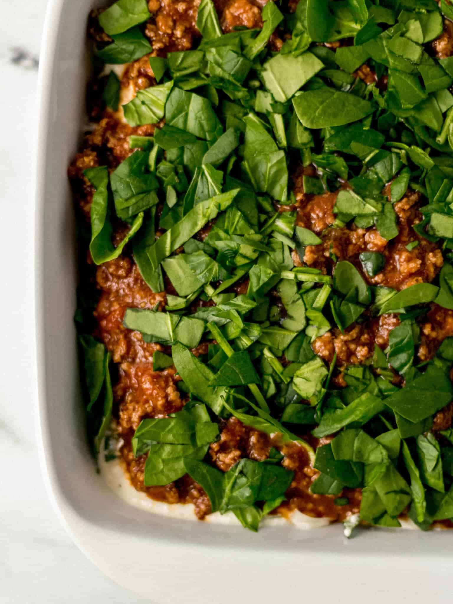 spinach added on top of the meat sauce in the baking dish 