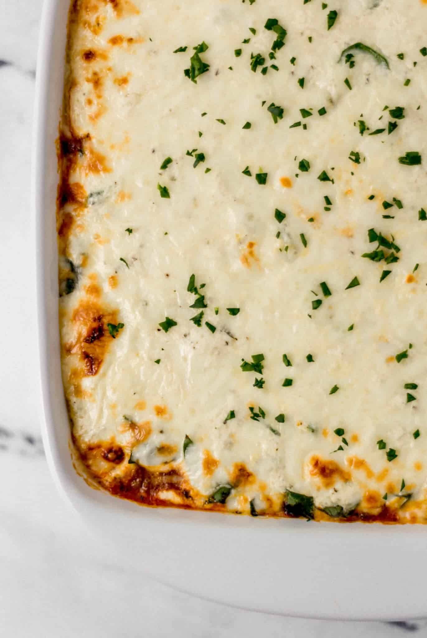 close up of finished lasagna topped with chopped parsley in white baking dish 