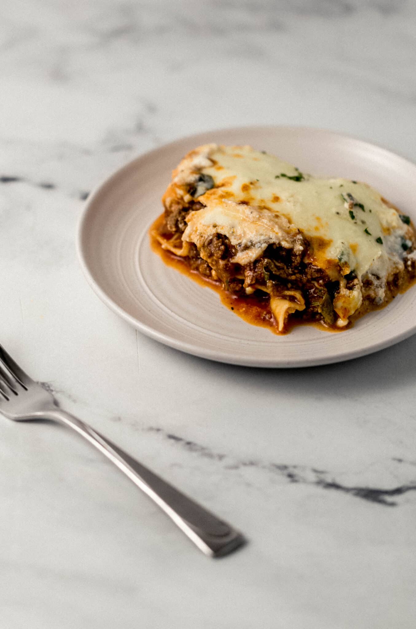 single serving of lasagna on white plate beside a fork 