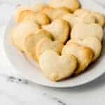 close up side view of white plate of heart shaped shortbread cookies