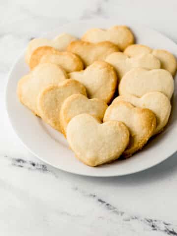 close up side view of white plate of heart shaped shortbread cookies